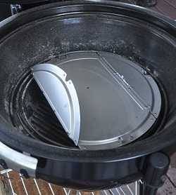 Black charcoal grill with lid up. A shiny metal disc is at the bottom.