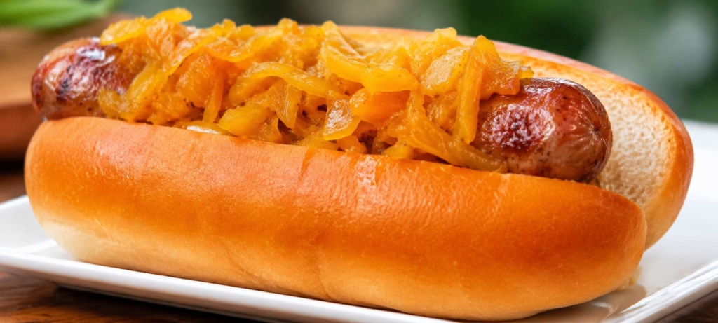 Grilled bratwurst on bun with onions on a white plate.