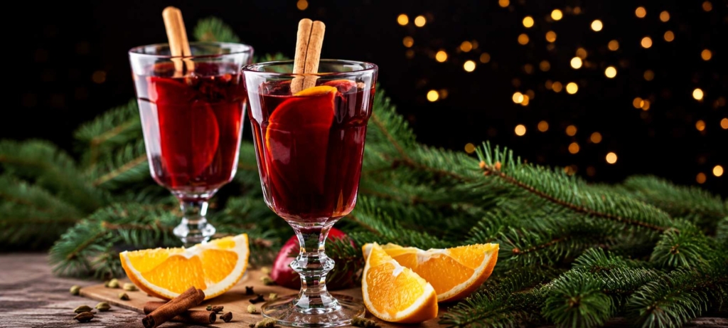 Swedish glogg mulled red wine in glass cups with cinnamon sticks and oranges with a Christmas background.