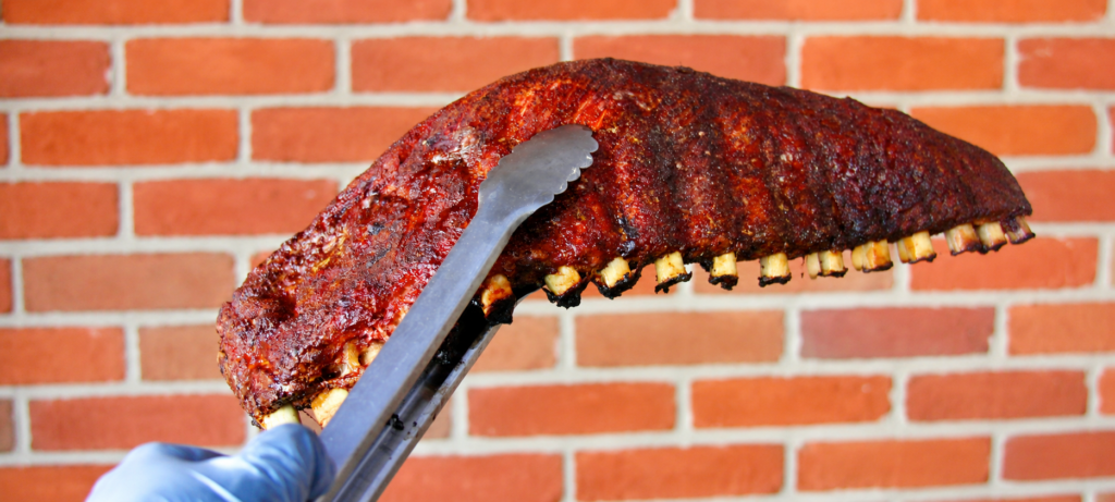 Smoked rack of ribs held by tongs