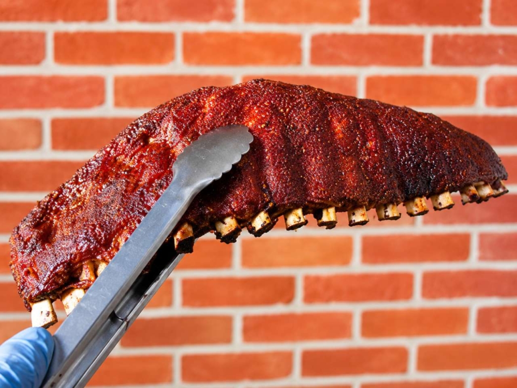 A rack of smoked ribs being held by tongs.