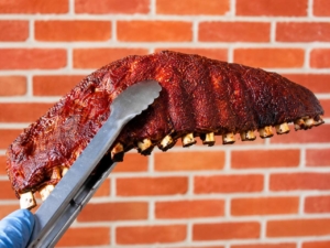 A rack of smoked ribs being held by tongs.