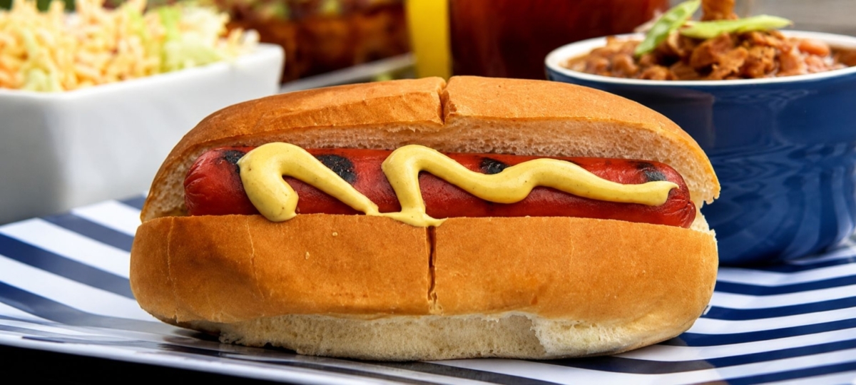Hot dog with mustard on striped plate.