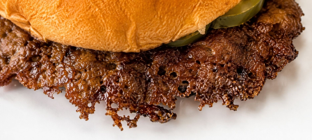 Crispy edges of a smash burger shown protuding from a hamburger bun.