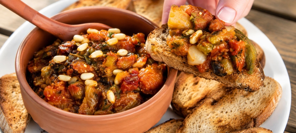 Eggplant caponata in a bowl and on a piece of tasted bread.
