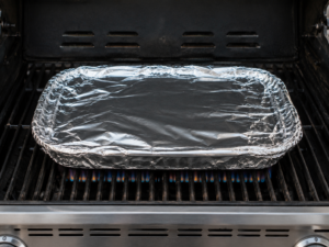 Lasagna wrapped in aluminium foil on a grill.