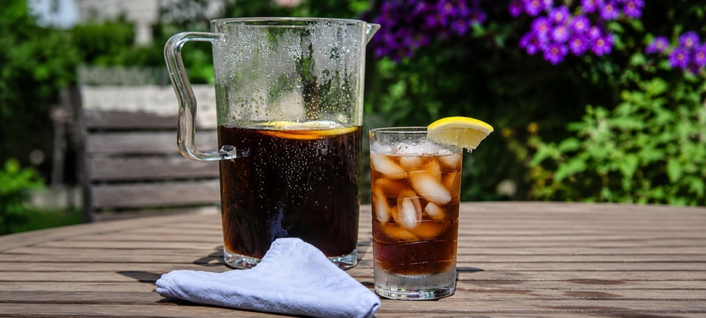 Pitcher and glass of sweet iced tea and blue napkin on a wooden outdoor table.