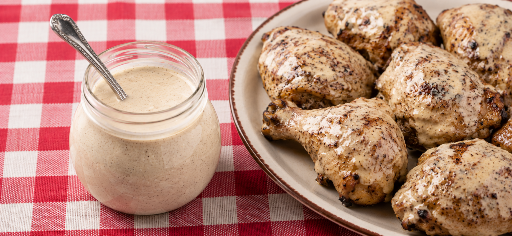 A jar of Alabama white BBQ sauce and a platter of grilled chicken brushed with the sauce