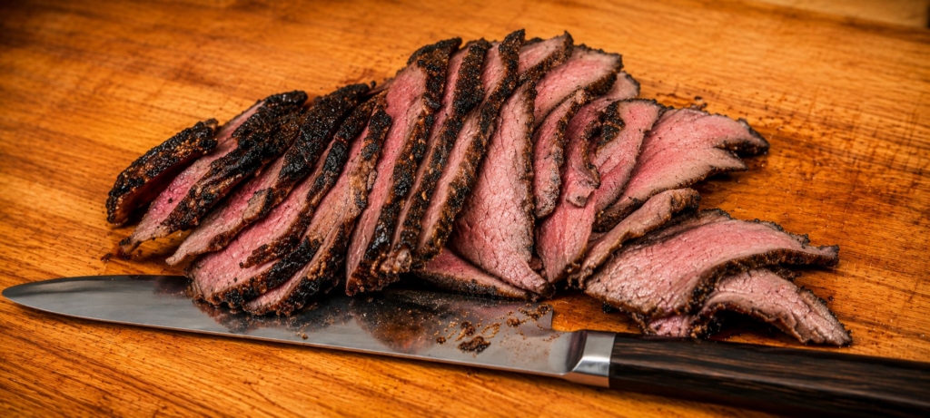 Sliced sous-vide-que bottom round roast on a cutting board with a knife.