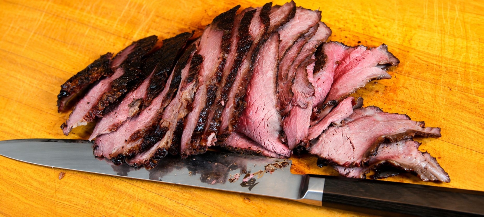 Sliced sous-vide-que bottom round roast on a cutting board with a knife
