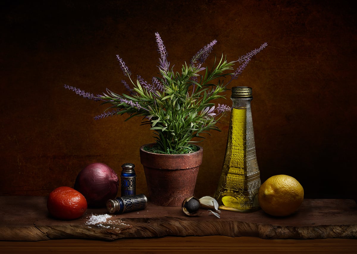 Marinade ingredients, including herbs, olive oil, lemon, garlic, onions, and salt, artfully arranged on a wooden table like a still life.