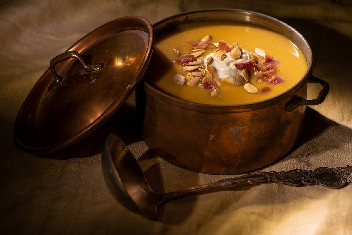 Smoked Squash Bisque in a copper pot with a ladle on a table.