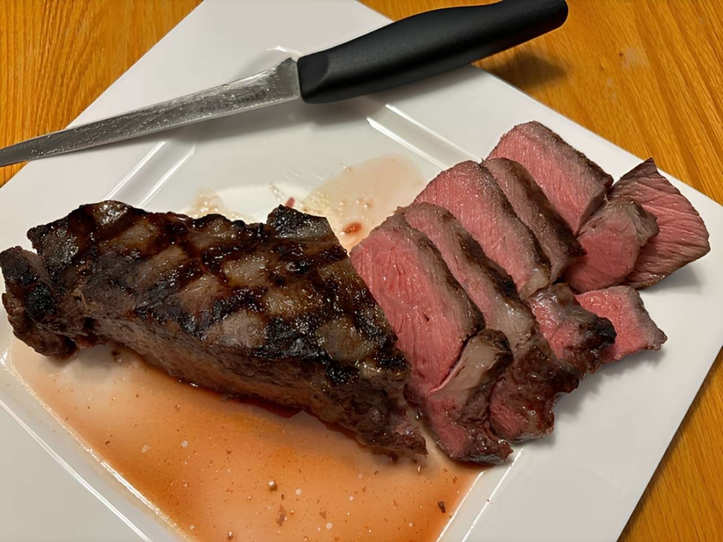Sliced steak and juices with a knife on a white plate