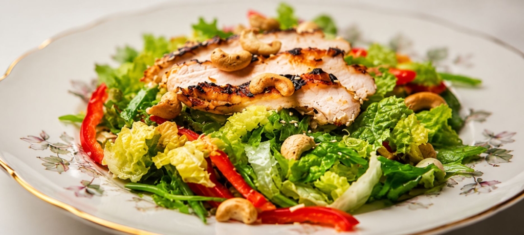 Salad topped with sliced turkey, red bell peppers, and cashews.
