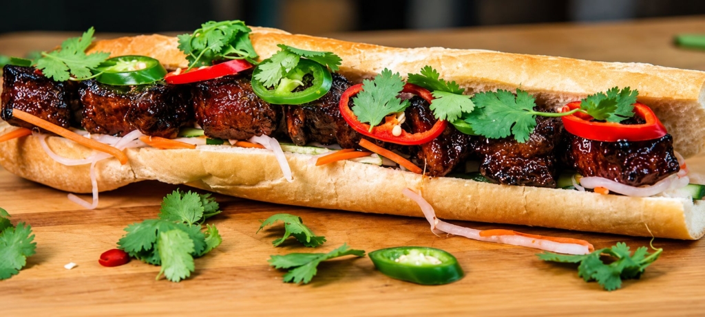 Pork belly banh mi with baguette, split and filled with meat, red and green jalapenos, and garnished with cilantro