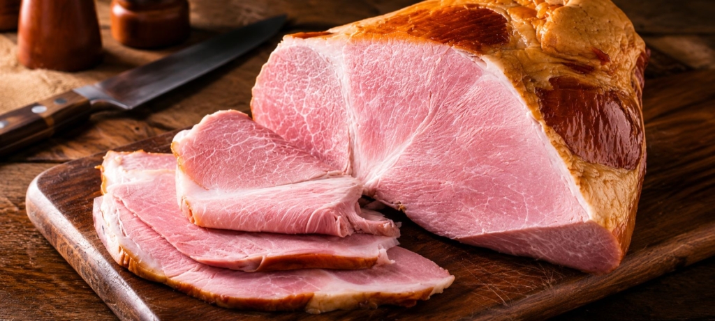 Homemade smoked ham sliced on a cutting board.