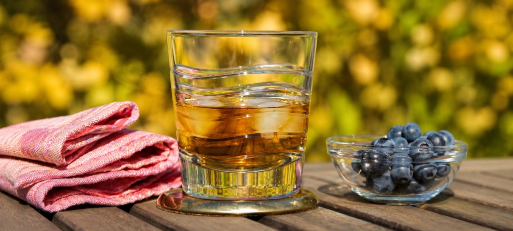 Smoked cocktail in glass rocks glass alongside a napkin and bowl of blueberries on a wood table