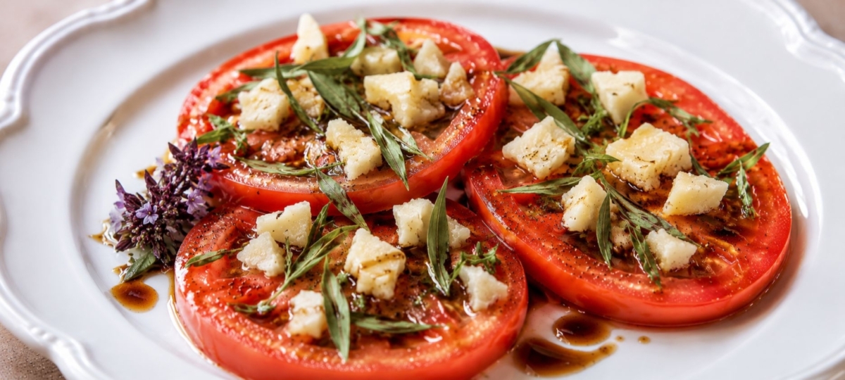 Parmesan cheese and basil leaves adorn red tomato slices on a white plate.