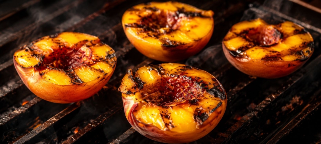 Four grilled peach halves on a grill grate.