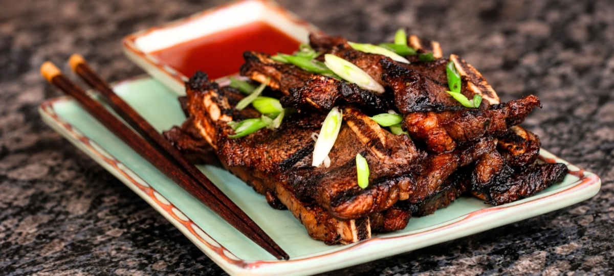 Grilled Korean style beef short ribs topped with green onion with a side dish of sweet chili dipping sauce and chopsticks