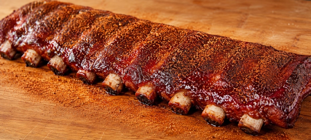 A rack of Memphis dry rubbed ribs dusted with rub and set on a wood cutting board.