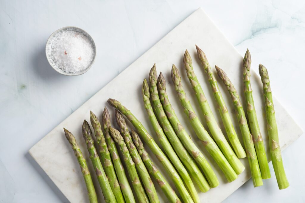 fresh asparagus on a cutting board near a small bowl of salt.