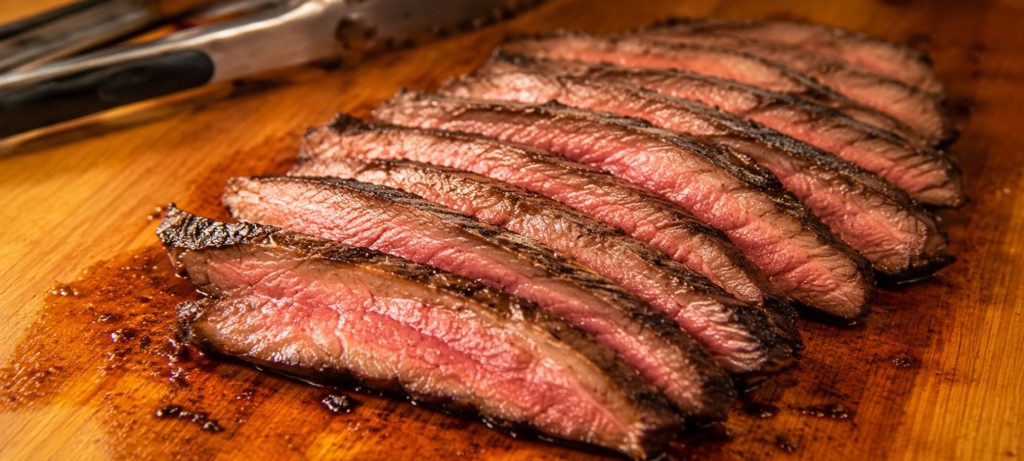 Sliced flank steak on a cutting board with tongs.