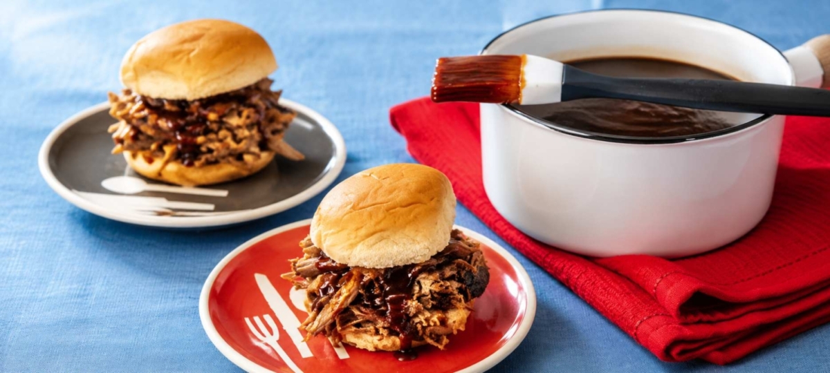 Tennessee whiskey BBQ sauce in a pot and on a sauce brush next two two plated pulled pork sandwiches