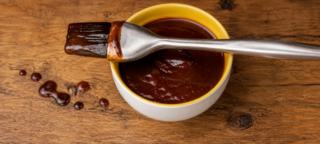 Overhead photo of BBQ sauce in a open container with a sauce brush laying across it