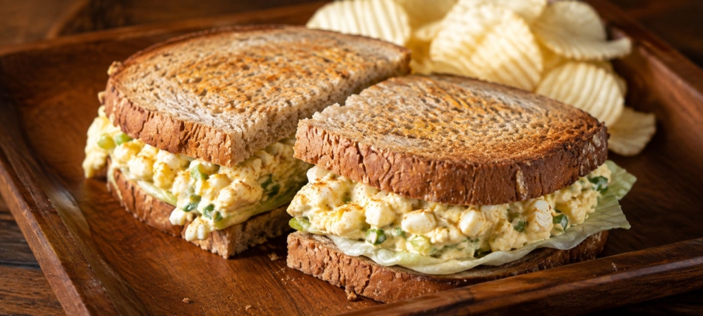 Egg salad sandwich cut in half and plated with potato chips.