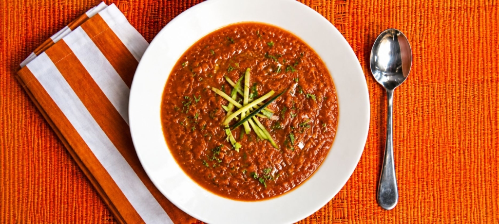 Gazpacho soup with matchstick cucumbers, and parsley in a white bowl.