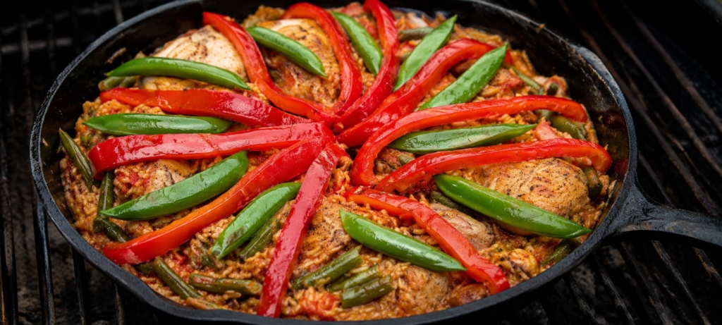 Paella in a cast iron skillet and topped with strips of red and green bell pepper.