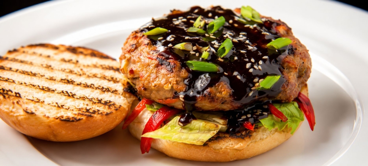 Burger covered in sauce, sitting on a bun with lettuce and tomato.