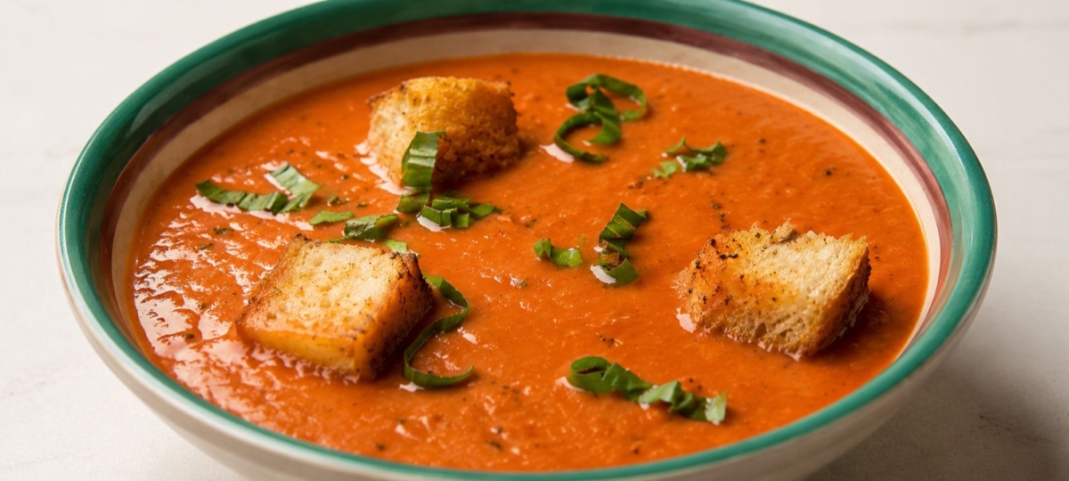 Smoked tomato soup in a bowl with croutons and basil.