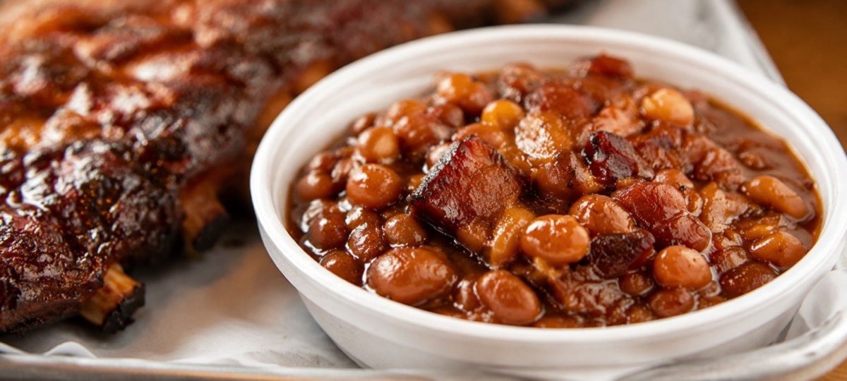 BBQ baked beans in a white bowl plated next to smoked ribs