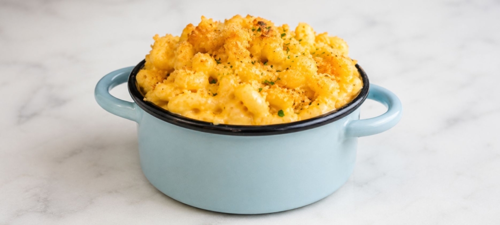 Mac-and-cheese in a blue metal bowl with handles on a white marble table.