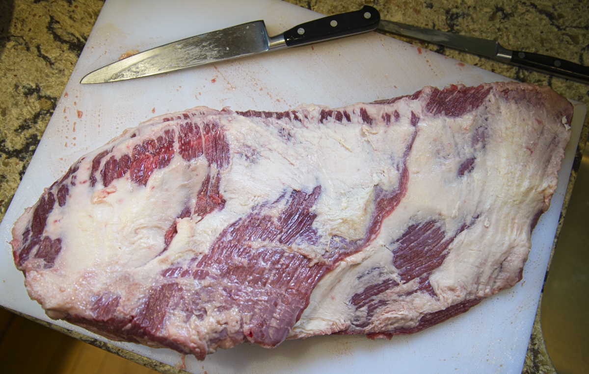 raw whole packer brisket shown fat side up on a white cutting board with a knife.