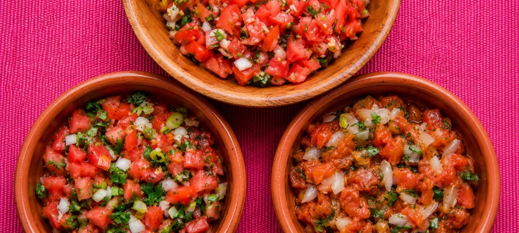 Three bowls of salsa on a red tablecloth