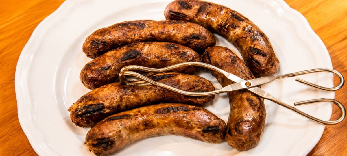 Grilled lamb merguez sausages on white plate with tongs.