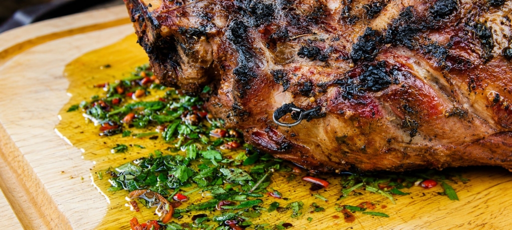Cooked leg of lamb on a cutting board with oil, chopped herb and chile board sauce