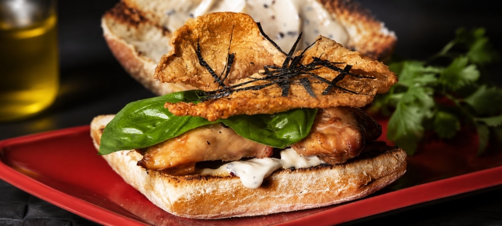 Chicken skin and chicken thigh sandwich with basil leaves.
