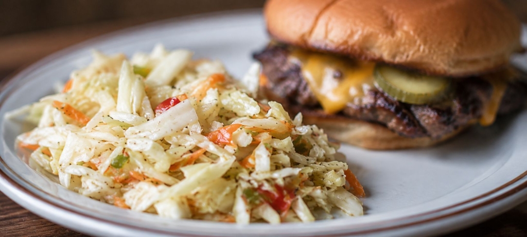 Sweet and sour coleslaw on a plate with a smash burger