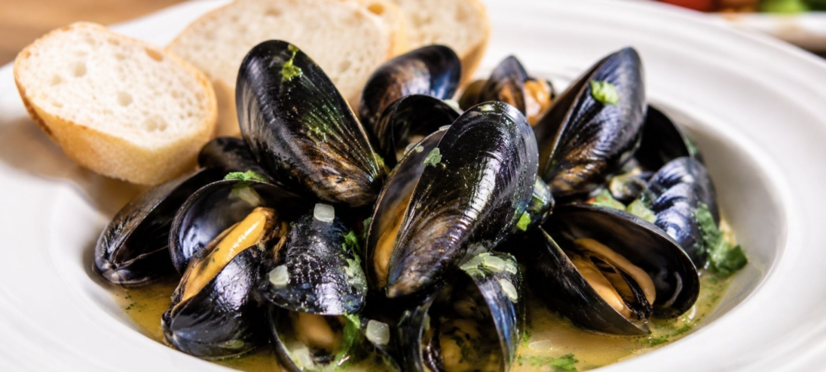 Mussels in a pile in a bowl and slices of bread.