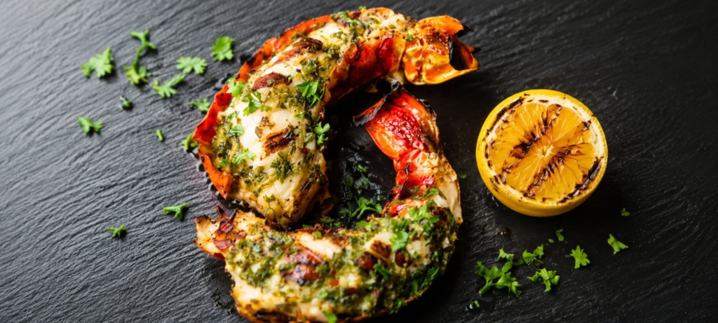 Grilled split lobster tail plated alongside a grilled lemon half
