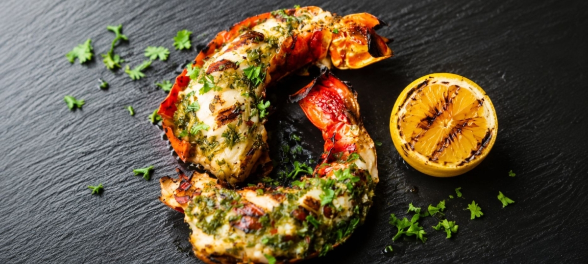 Grilled split lobster tail plated alongside a grilled lemon half