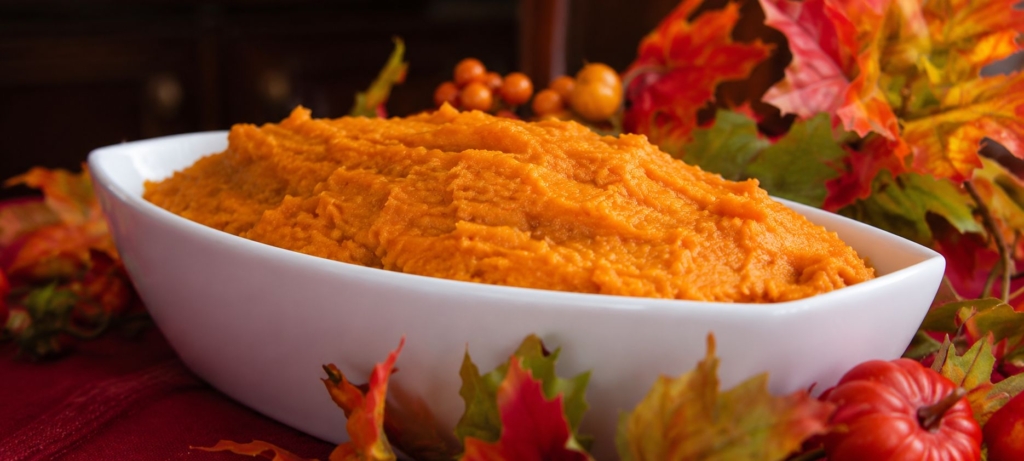 Mashed sweet potatoes in a white bowl surrounded by fall leaves.
