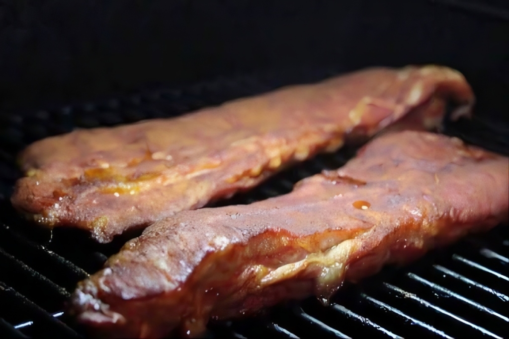 ribs tips recipe showing ribs smoking on cooking grates.