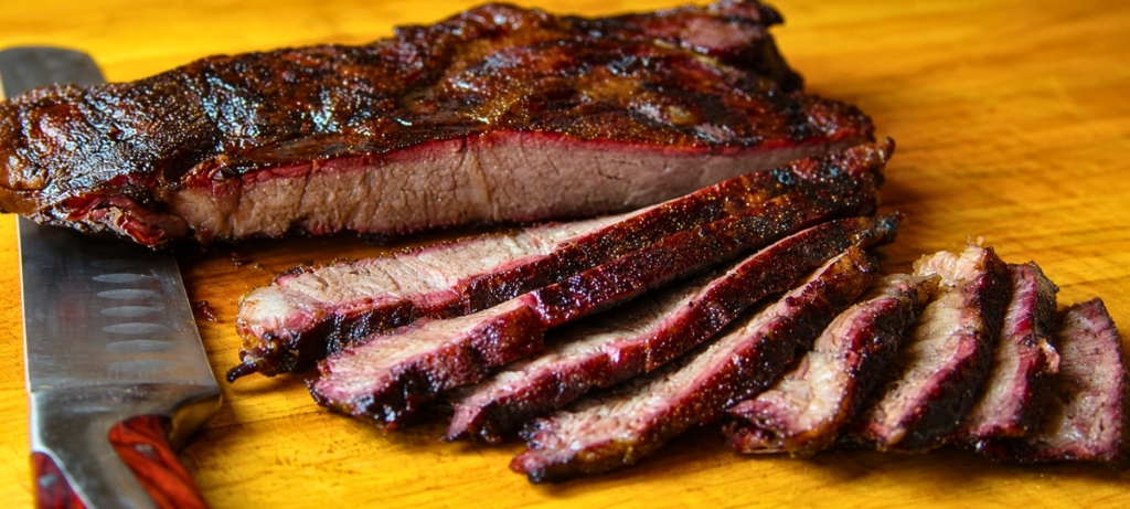 Smoked sliced chuck roast next to a slicing knife.