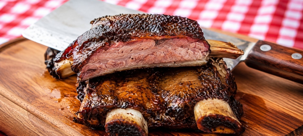Smoked and sliced beef ribs on cutting board with cleaver.