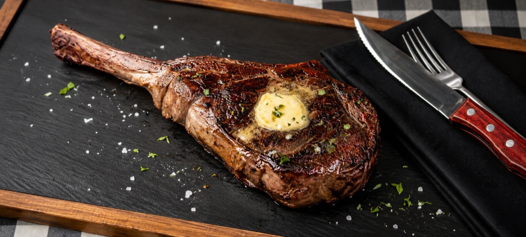 Grilled tomahawk bison ribeye steak on a slate board.